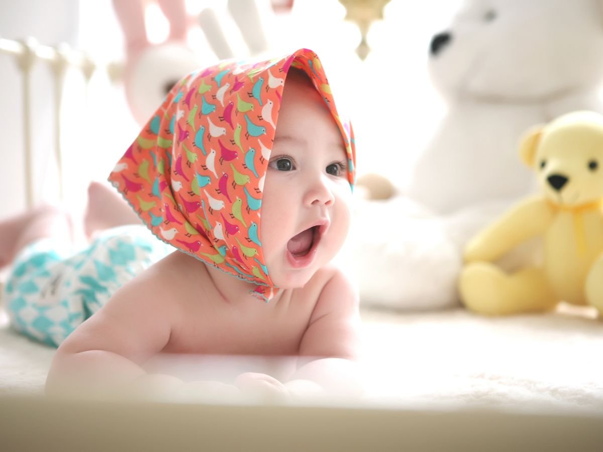Smiling baby lying on a soft nursery bed beside teddy bears