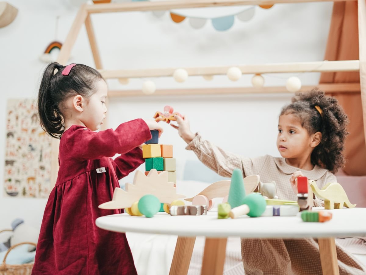 Two toddlers building with colourful wooden blocks in a playroom