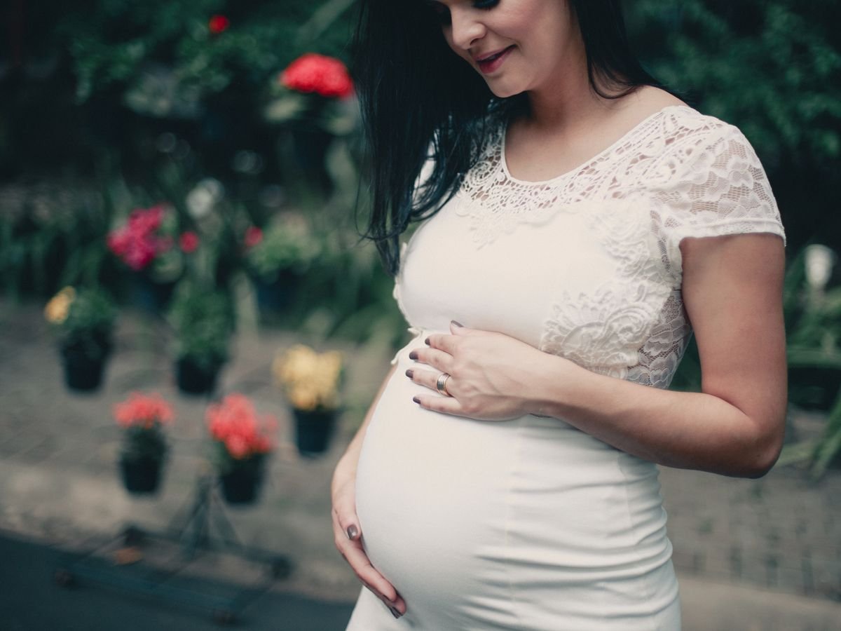 Expectant mother in a white lace dress gently holding her bump